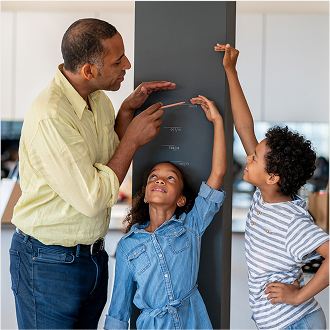A father helping his children measure their growth, knowing his family is protected with variable universal life insurance.